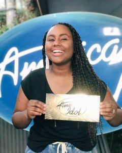 Jamie Grace Harper standing in front of the American Idol logo backdrop, holding her golden ticket, sending her to Hollywood